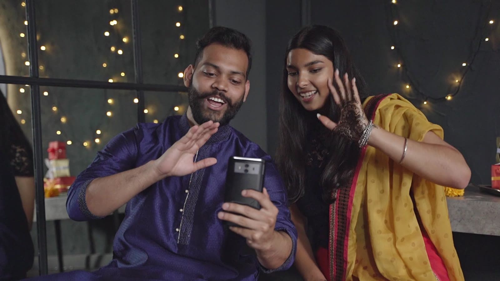 Two friends in festive wear smiling at a phone